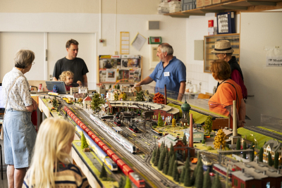 Erwachsene und Kinder bestaunen eine Modelleisenbahnlandschaft.